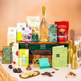 EDEN & CO. Luxury Wicker Hamper filled with a full-size Bottega Gold prosecco, an assortment of chocolate bars, Booja-Booja Chocolate Wonders truffles and Buttermilk snack bars, presented in a dark green trimmed wicker basket with an “Occasion Themed” card, styled against a warm terracotta background.