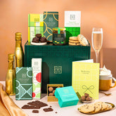 EDEN & CO. Chocolate Hamper letterbox gift with a mini Bottega Gold prosecco, green gift tube, an “Occasion Themed” card, an assortment of chocolate bars, Booja-Booja Chocolate Wonders truffles and chocolate truffles on a small plate, styled against a warm terracotta background.