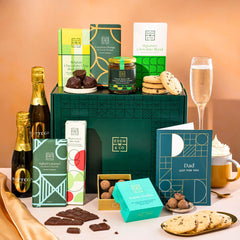 EDEN & CO. Chocolate Hamper letterbox gift with a mini Bottega Zero Black prosecco (0% alcohol-free), green gift tube, an “Occasion Themed” card, an assortment of chocolate bars, Booja-Booja Chocolate Wonders truffles and chocolate truffles on a small plate, styled against a warm terracotta background.