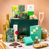 EDEN & CO. Chocolate Hamper letterbox gift with a mini Bottega Gold prosecco, green gift tube, an “Occasion Themed” card, an assortment of chocolate bars, Booja-Booja Chocolate Wonders truffles and chocolate truffles on a small plate, styled against a warm terracotta background.