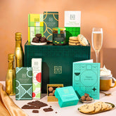 EDEN & CO. Chocolate Hamper letterbox gift with a mini Bottega Gold prosecco, green gift tube, an “Occasion Themed” card, an assortment of chocolate bars, Booja-Booja Chocolate Wonders truffles and chocolate truffles on a small plate, styled against a warm terracotta background.