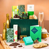 EDEN & CO. Chocolate Hamper letterbox gift with a mini Bottega Gold prosecco, green gift tube, an “Occasion Themed” card, an assortment of chocolate bars, Booja-Booja Chocolate Wonders truffles and chocolate truffles on a small plate, styled against a warm terracotta background.