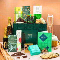EDEN & CO. Chocolate Hamper letterbox gift with a mini Bottega Zero Black prosecco (0% alcohol-free), green gift tube, an “Occasion Themed” card, an assortment of chocolate bars, Booja-Booja Chocolate Wonders truffles and chocolate truffles on a small plate, styled against a warm terracotta background.