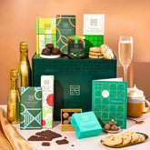EDEN & CO. Chocolate Hamper letterbox gift with a mini Bottega Gold prosecco, green gift tube, an “Occasion Themed” card, an assortment of chocolate bars, Booja-Booja Chocolate Wonders truffles and chocolate truffles on a small plate, styled against a warm terracotta background.