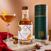 EDEN & CO. liqueur gift bottle with an “Occasion Themed” card, presented in a branded gift tube, styled with gold silk against a warm terracotta background.