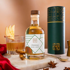 EDEN & CO. liqueur gift bottle with an “Occasion Themed” card, presented in a branded gift tube, styled with gold silk against a warm terracotta background.
