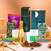 EDEN & CO. plant-based gift hamper with a mini Bottega Gold prosecco, green gift tube, “Occasion Themed” card, chocolate bars in Luscious Orange, White Chocolate Velvet, Signature Chocolate Blend and Salted Caramel, Booja-Booja Chocolate Wonders truffles, Buttermilk Peanut Nougat and Honeycomb Blast bars, chocolate truffles and honeycomb pieces on small plates, and a filled champagne glass, set against a warm terracotta background.