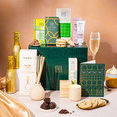 EDEN & CO. Pamper Hamper gift set with a mini Bottega Gold prosecco, dark green gift cylinder, an “Occasion Themed” card, chocolate bars and truffles, a scented candle and Aery hand cream, styled with gold silk against a warm terracotta background.