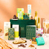 EDEN & CO. Hamper Gift Subscription box with a full-size Bottega Gold prosecco, dark green gift cylinder, an “Occasion Themed” card, a rotating selection of chocolates, truffles and treats, styled with gold silk against a warm terracotta background.