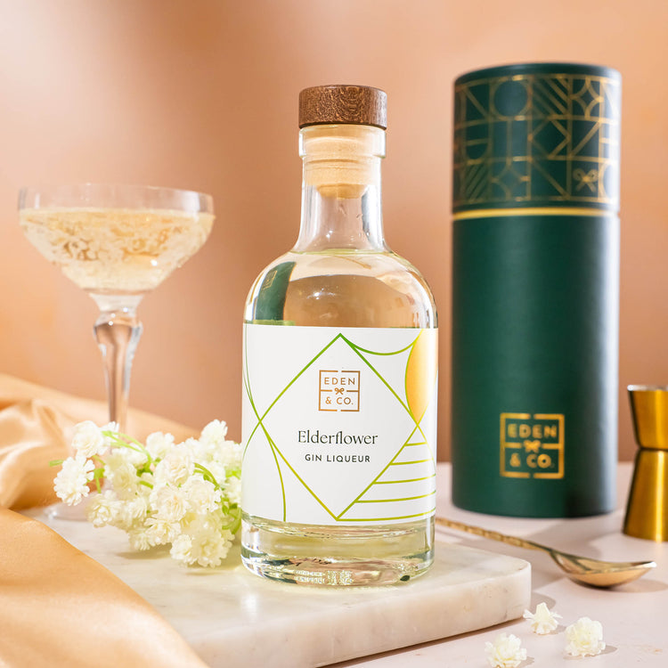 EDEN & CO. liqueur gift bottle with an “Occasion Themed” card, presented in a branded gift tube, styled with gold silk against a warm terracotta background.