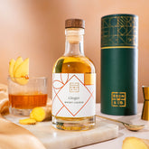 EDEN & CO. liqueur gift bottle with an “Occasion Themed” card, presented in a branded gift tube, styled with gold silk against a warm terracotta background.