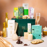EDEN & CO. Pamper Hamper gift set with a mini Bottega Gold prosecco, dark green gift cylinder, an “Occasion Themed” card, chocolate bars and truffles, a scented candle and Aery hand cream, styled with gold silk against a warm terracotta background.