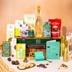 EDEN & CO. Luxury Wicker Hamper filled with a full-size Bottega Gold prosecco, an assortment of chocolate bars, Booja-Booja Chocolate Wonders truffles and Buttermilk snack bars, presented in a dark green trimmed wicker basket with an “Occasion Themed” card, styled against a warm terracotta background.