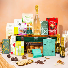 EDEN & CO. Luxury Wicker Hamper filled with a full-size Bottega Zero Black prosecco (0% alcohol-free), an assortment of chocolate bars, Booja-Booja Chocolate Wonders truffles and Buttermilk snack bars, presented in a dark green trimmed wicker basket with an “Occasion Themed” card, styled against a warm terracotta background.