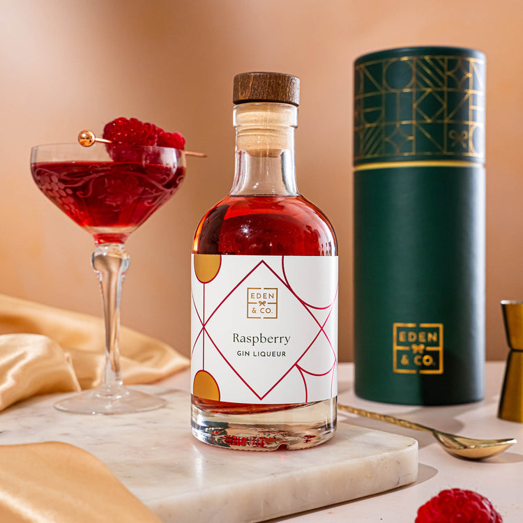 EDEN & CO. liqueur gift bottle with an “Occasion Themed” card, presented in a branded gift tube, styled with gold silk against a warm terracotta background.