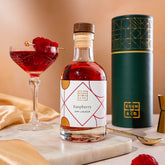 EDEN & CO. liqueur gift bottle with an “Occasion Themed” card, presented in a branded gift tube, styled with gold silk against a warm terracotta background.