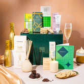 EDEN & CO. Pamper Hamper gift set with a mini Bottega Gold prosecco, dark green gift cylinder, an “Occasion Themed” card, chocolate bars and truffles, a scented candle and Aery hand cream, styled with gold silk against a warm terracotta background.