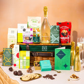 EDEN & CO. Luxury Wicker Hamper filled with a full-size Bottega Gold prosecco, an assortment of chocolate bars, Booja-Booja Chocolate Wonders truffles and Buttermilk snack bars, presented in a dark green trimmed wicker basket with an “Occasion Themed” card, styled against a warm terracotta background.