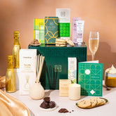 EDEN & CO. Pamper Hamper gift set with a mini Bottega Gold prosecco, dark green gift cylinder, an “Occasion Themed” card, chocolate bars and truffles, a scented candle and Aery hand cream, styled with gold silk against a warm terracotta background.