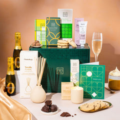 EDEN & CO. Pamper Hamper gift set with a mini Bottega Zero Black prosecco (0% alcohol-free), dark green gift cylinder, an “Occasion Themed” card, chocolate bars and truffles, a scented candle and Aery hand cream, styled with gold silk against a warm terracotta background.