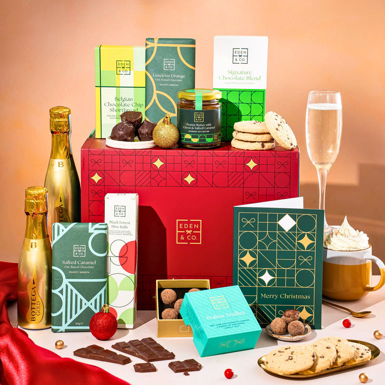 EDEN & CO. Chocolate Hamper letterbox gift with a mini Bottega Gold prosecco, green gift tube, an “Occasion Themed” card, an assortment of chocolate bars, Booja-Booja Chocolate Wonders truffles and chocolate truffles on a small plate, styled against a warm terracotta background.