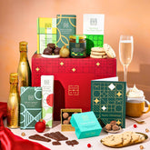 EDEN & CO. Chocolate Hamper letterbox gift with a mini Bottega Gold prosecco, green gift tube, an “Occasion Themed” card, an assortment of chocolate bars, Booja-Booja Chocolate Wonders truffles and chocolate truffles on a small plate, styled against a warm terracotta background.
