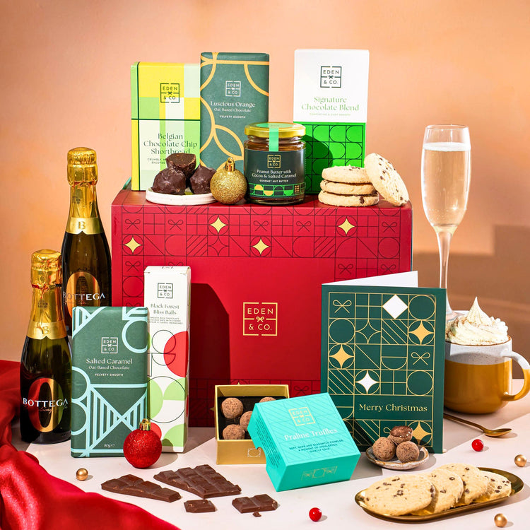 EDEN & CO. Chocolate Hamper letterbox gift with a mini Bottega Zero Black prosecco (0% alcohol-free), green gift tube, an “Occasion Themed” card, an assortment of chocolate bars, Booja-Booja Chocolate Wonders truffles and chocolate truffles on a small plate, styled against a warm terracotta background.