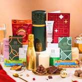 EDEN & CO. plant-based gift hamper with a mini Bottega Gold prosecco, green gift tube, “Occasion Themed” card, chocolate bars in Luscious Orange, White Chocolate Velvet, Signature Chocolate Blend and Salted Caramel, Booja-Booja Chocolate Wonders truffles, Buttermilk Peanut Nougat and Honeycomb Blast bars, chocolate truffles and honeycomb pieces on small plates, and a filled champagne glass, luxury candle and hand cream set against a warm terracotta background.