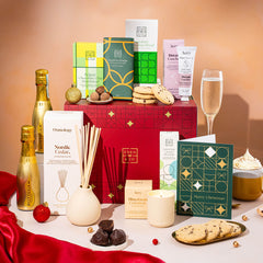 EDEN & CO. Pamper Hamper gift set with a mini Bottega Gold prosecco, dark green gift cylinder, an “Occasion Themed” card, chocolate bars and truffles, a scented candle and Aery hand cream, styled with gold silk against a warm terracotta background.
