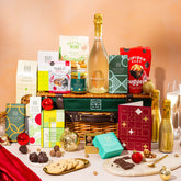 EDEN & CO. Luxury Wicker Hamper filled with a full-size Bottega Gold prosecco, an assortment of chocolate bars, Booja-Booja Chocolate Wonders truffles and Buttermilk snack bars, presented in a dark green trimmed wicker basket with an “Occasion Themed” card, styled against a warm terracotta background.