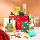 EDEN & CO. Food & Drink Hamper with a full-size Bottega Gold prosecco, dark green gift cylinder, an “Occasion Themed” card, an assortment of chocolate bars, Booja-Booja Chocolate Wonders truffles, Buttermilk snack bars, a scented candle and Aery hand cream, styled with gold silk against a warm terracotta background.