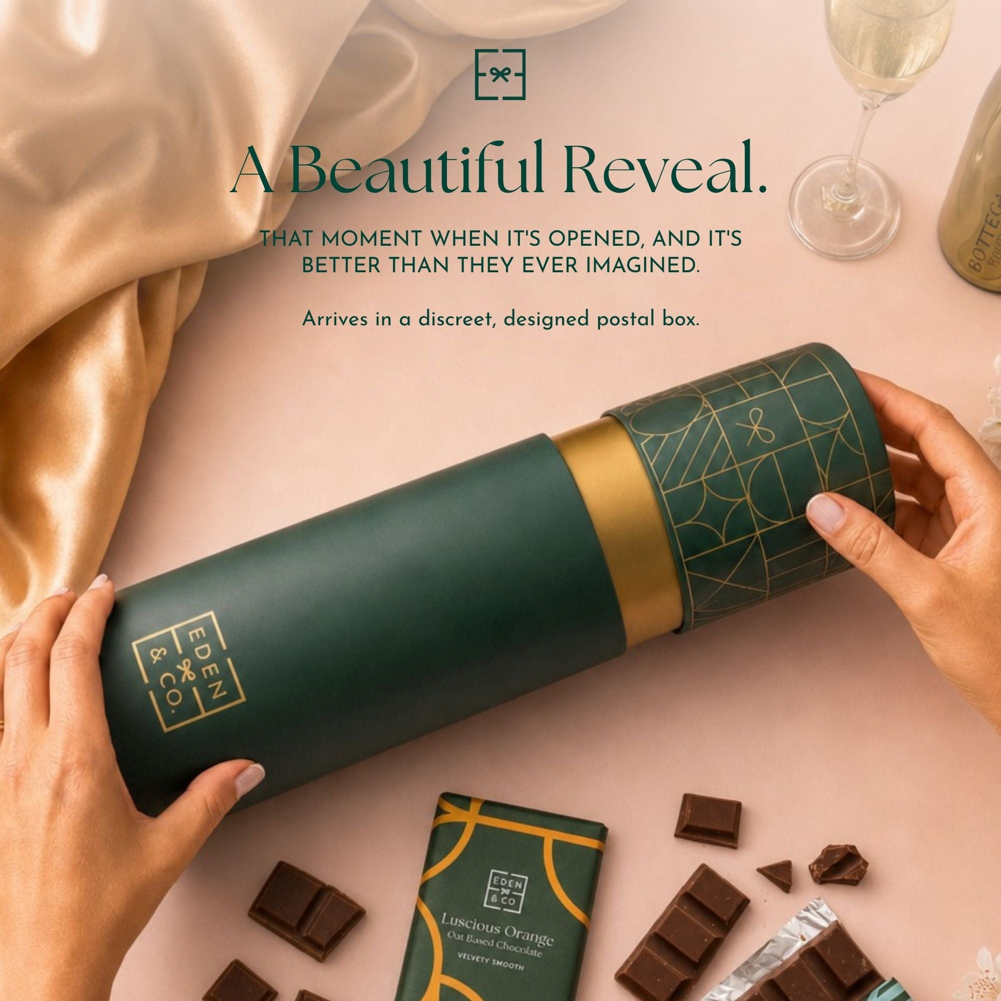 Unboxing: EDEN & CO. gift tube being opened by hand, headline “A Beautiful Reveal” with text “That moment when it’s opened, and it’s better than they ever imagined. Arrives in a discreet, designed postal box,” styled with gold silk, champagne and chocolate pieces.