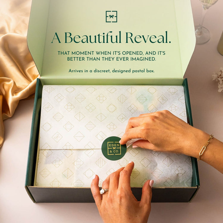 Unboxing: Hands placing an EDEN & CO. branded sticker on gold-patterned tissue paper inside an open sage green gift box, headline “A Beautiful Reveal” with text “That moment when it’s opened, and it’s better than they ever imagined. Arrives in a discreet, designed postal box.”