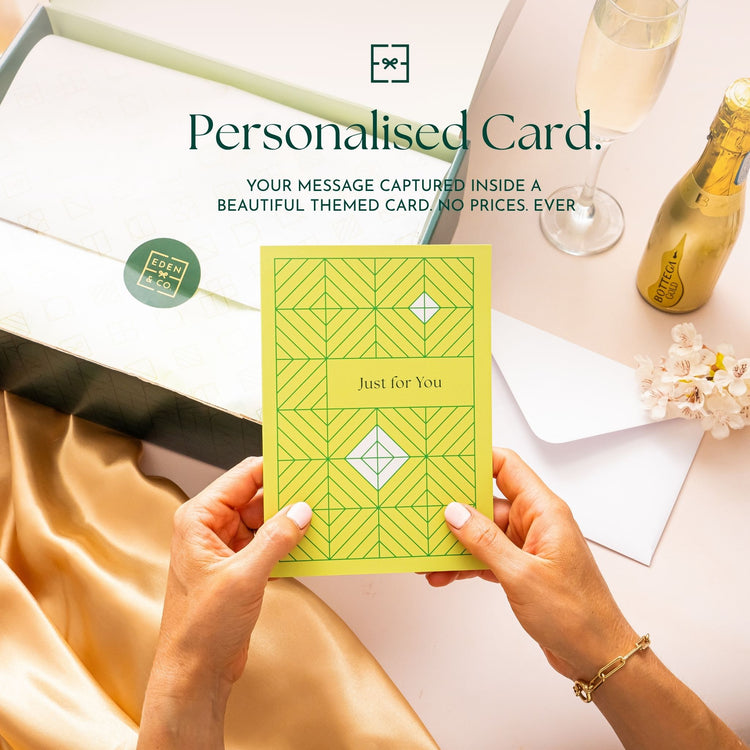 Personalised Card: Hands holding a yellow geometric-patterned “Just for You” card above an open EDEN & CO. gift box, headline “Personalised Card” with text “Your message captured inside a beautiful themed card. No prices. Ever,” styled with champagne, gold silk and flowers.