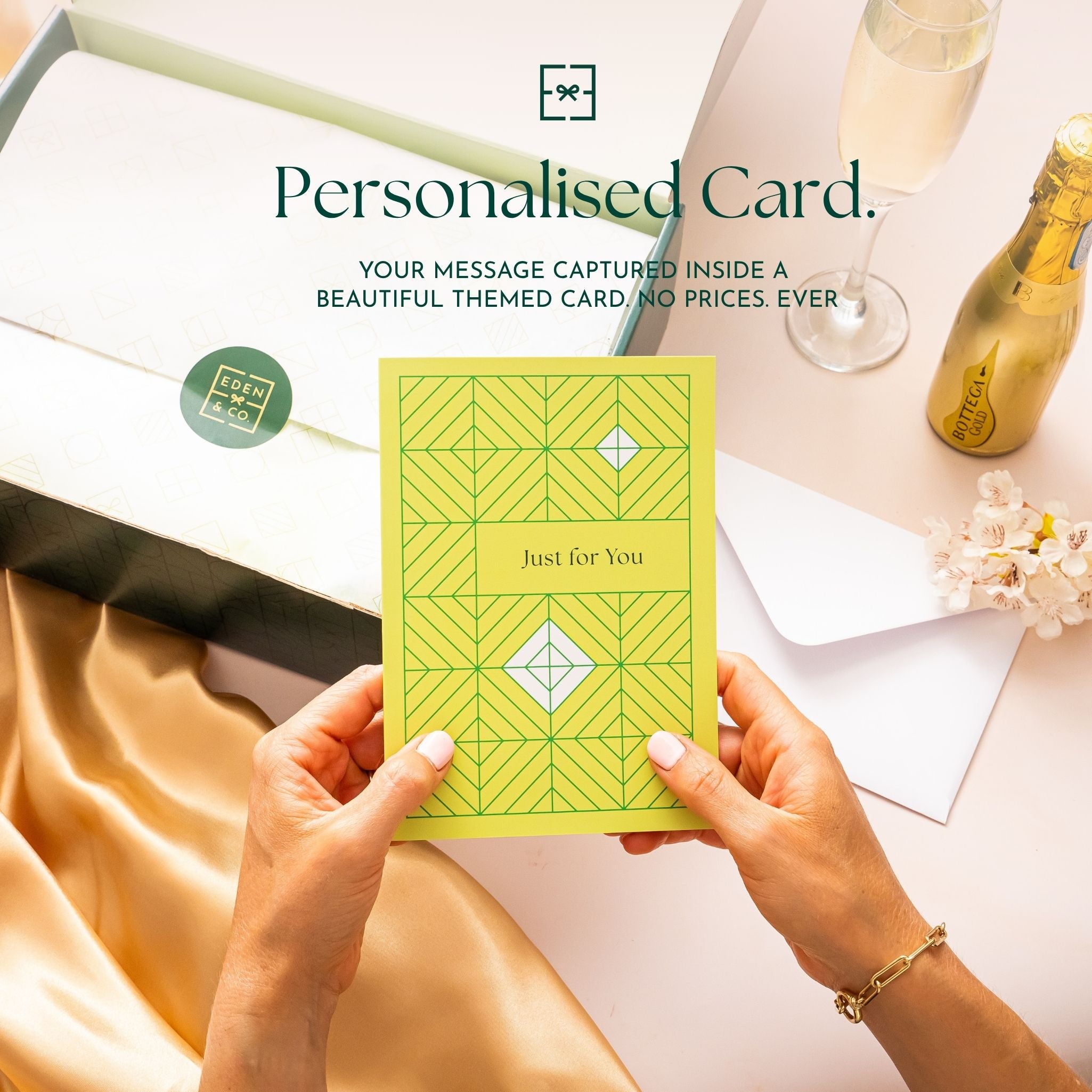 Personalised Card: Hands holding a yellow geometric-patterned “Just for You” card above an open EDEN & CO. gift box, headline “Personalised Card” with text “Your message captured inside a beautiful themed card. No prices. Ever,” styled with champagne, gold silk and flowers.