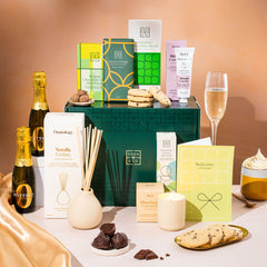 EDEN & CO. Pamper Hamper gift set with a mini Bottega Zero Black prosecco (0% alcohol-free), dark green gift cylinder, an “Occasion Themed” card, chocolate bars and truffles, a scented candle and Aery hand cream, styled with gold silk against a warm terracotta background.
