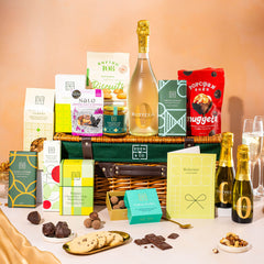 EDEN & CO. Luxury Wicker Hamper filled with a full-size Bottega Zero Black prosecco (0% alcohol-free), an assortment of chocolate bars, Booja-Booja Chocolate Wonders truffles and Buttermilk snack bars, presented in a dark green trimmed wicker basket with an “Occasion Themed” card, styled against a warm terracotta background.