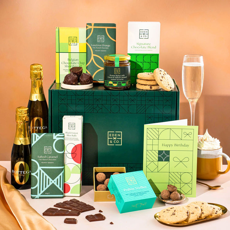 EDEN & CO. Chocolate Hamper letterbox gift with a mini Bottega Zero Black prosecco (0% alcohol-free), green gift tube, an “Occasion Themed” card, an assortment of chocolate bars, Booja-Booja Chocolate Wonders truffles and chocolate truffles on a small plate, styled against a warm terracotta background.