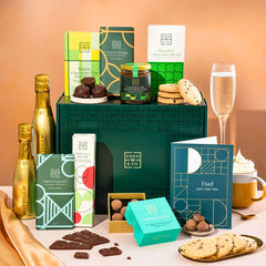 EDEN & CO. Chocolate Hamper letterbox gift with a mini Bottega Gold prosecco, green gift tube, an “Occasion Themed” card, an assortment of chocolate bars, Booja-Booja Chocolate Wonders truffles and chocolate truffles on a small plate, styled against a warm terracotta background.