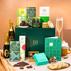 EDEN & CO. Chocolate Hamper letterbox gift with a mini Bottega Zero Black prosecco (0% alcohol-free), green gift tube, an “Occasion Themed” card, an assortment of chocolate bars, Booja-Booja Chocolate Wonders truffles and chocolate truffles on a small plate, styled against a warm terracotta background.
