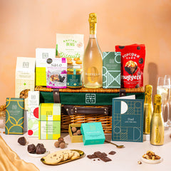 EDEN & CO. Luxury Wicker Hamper filled with a full-size Bottega Gold prosecco, an assortment of chocolate bars, Booja-Booja Chocolate Wonders truffles and Buttermilk snack bars, presented in a dark green trimmed wicker basket with an “Occasion Themed” card, styled against a warm terracotta background.