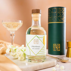 EDEN & CO. liqueur gift bottle with an “Occasion Themed” card, presented in a branded gift tube, styled with gold silk against a warm terracotta background.