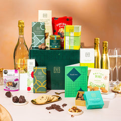 EDEN & CO. Grand Hamper gift box with a full-size Bottega Gold prosecco, dark green gift cylinder, an “Occasion Themed” card, an assortment of chocolate bars, Booja-Booja Chocolate Wonders truffles and Buttermilk snack bars, styled with gold silk against a warm terracotta background.