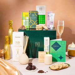 EDEN & CO. Pamper Hamper gift set with a mini Bottega Gold prosecco, dark green gift cylinder, an “Occasion Themed” card, chocolate bars and truffles, a scented candle and Aery hand cream, styled with gold silk against a warm terracotta background.