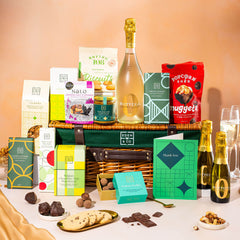 EDEN & CO. Luxury Wicker Hamper filled with a full-size Bottega Zero Black prosecco (0% alcohol-free), an assortment of chocolate bars, Booja-Booja Chocolate Wonders truffles and Buttermilk snack bars, presented in a dark green trimmed wicker basket with an “Occasion Themed” card, styled against a warm terracotta background.