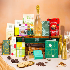 EDEN & CO. Luxury Wicker Hamper filled with a full-size Bottega Gold prosecco, an assortment of chocolate bars, Booja-Booja Chocolate Wonders truffles and Buttermilk snack bars, presented in a dark green trimmed wicker basket with an “Occasion Themed” card, styled against a warm terracotta background.