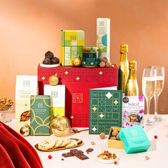 EDEN & CO. Food & Drink Hamper with a full-size Bottega Gold prosecco, dark green gift cylinder, an “Occasion Themed” card, an assortment of chocolate bars, Booja-Booja Chocolate Wonders truffles, Buttermilk snack bars, a scented candle and Aery hand cream, styled with gold silk against a warm terracotta background.