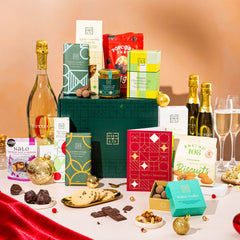 EDEN & CO. Grand Hamper gift box with a full-size Bottega Zero Black prosecco (0% alcohol-free), dark green gift cylinder, an “Occasion Themed” card, an assortment of chocolate bars, Booja-Booja Chocolate Wonders truffles and Buttermilk snack bars, styled with gold silk against a warm terracotta background.